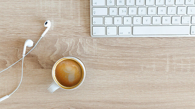 Bovenaanzicht van een bureaublad met een kop koffie, oortjes en een toetsenbord