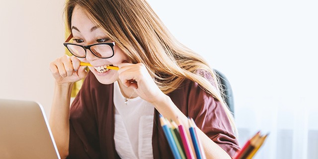 Een vrouw bijt op een potlood en kijkt naar een laptopscherm