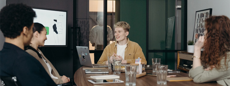 Vier collega's in overleg in een vergaderruimte aan een tafel met daarop glazen en werkspullen