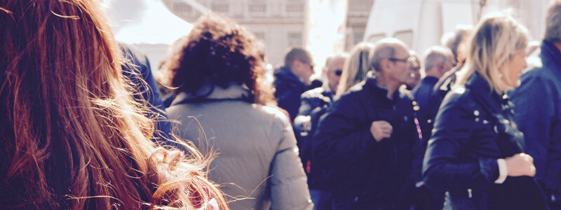 Achteraanzicht van een vrouw op een druk voetpad in de zon met mensen met jassen aan