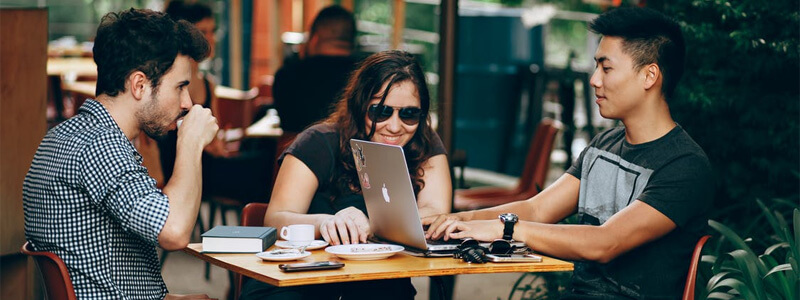 Drie mensen zitten buiten bij een café aan tafel met een laptop